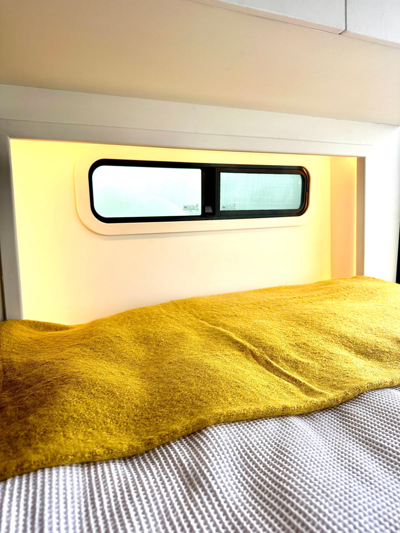 Cozy RV rental bed with a vibrant yellow blanket, built-in warm lighting, and compact windows. — photo 10