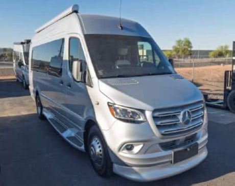Silver Mercedes-Benz Sprinter RV rental van, featuring an awning and running boards, parked outside on a sunny day.