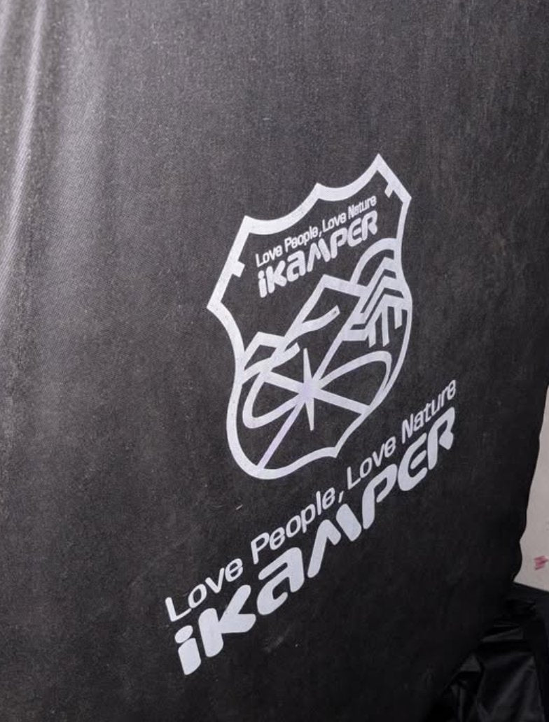 The included iKamper travel cover fitted over the closed tent, showing the printed shield crest and Love People, Love Nature wordmark on the black fabric — photo 3