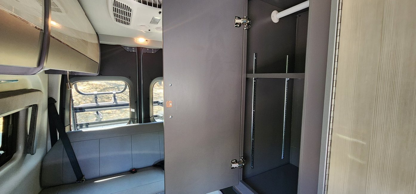 Inside an RV rental: a versatile closet with hanging rod & adjustable shelves, and a comfortable rear bench seat.