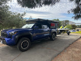 Blue pickup truck with camper, towing a jet ski at a lake campsite, ready for adventure. Explore our RV rental options!