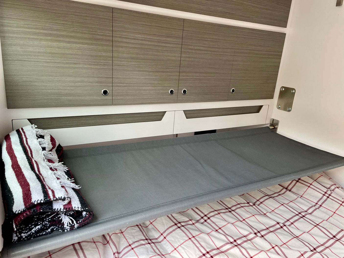 Compact RV rental interior with a grey mesh bunk bed, wood-grain cabinets, and plaid bedding, designed for efficient travel.
