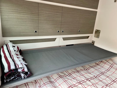 Compact RV rental interior with a grey mesh bunk bed, wood-grain cabinets, and plaid bedding, designed for efficient travel.