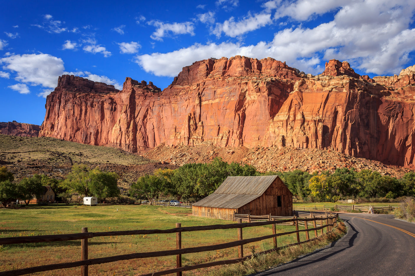 A historic barn, green fields, and majestic red cliffs, with a small camper. Perfect scenery for an unforgettable RV rental trip.