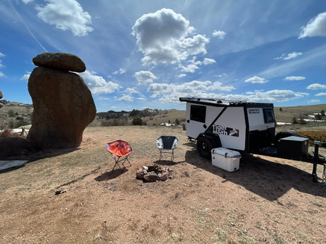 This scenic campsite features an off-road camper trailer, chairs, and fire pit, ideal for an RV rental outdoor adventure.