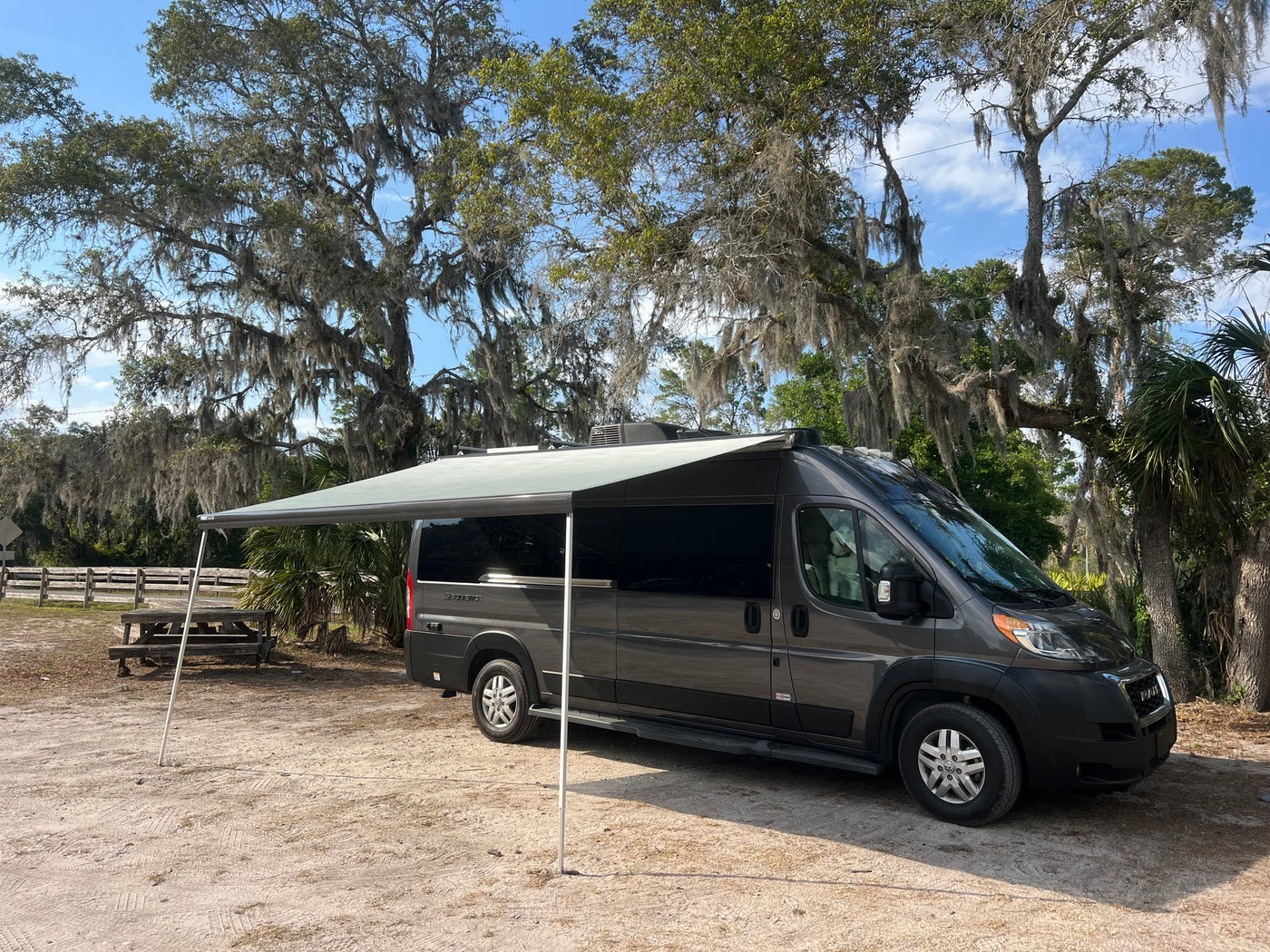  parked amidst moss-draped trees and blue skies.|Grey RV rental with awning extended — photo 2