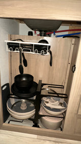 Efficiently organized kitchen essentials in an RV rental cabinet, featuring sink plumbing, stacked dishes, cookware, and hanging utensils.