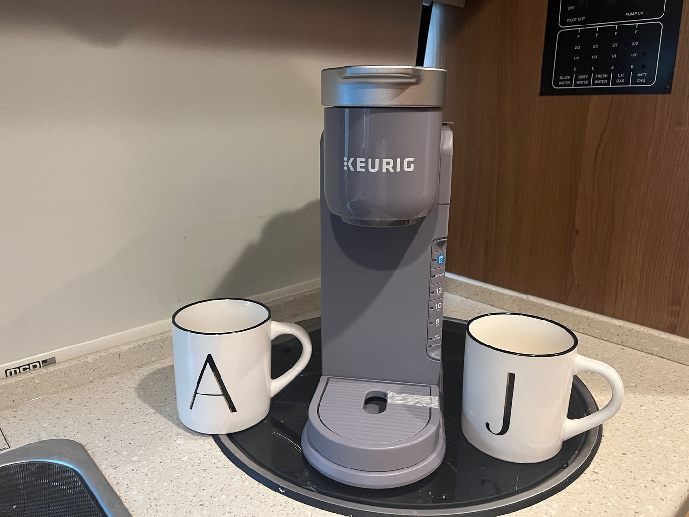 A gray Keurig coffee maker and mugs in an RV rental kitchen, with a utility panel visible. Perfect for a cozy brew on the go.