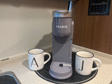 A gray Keurig coffee maker and mugs in an RV rental kitchen, with a utility panel visible. Perfect for a cozy brew on the go.