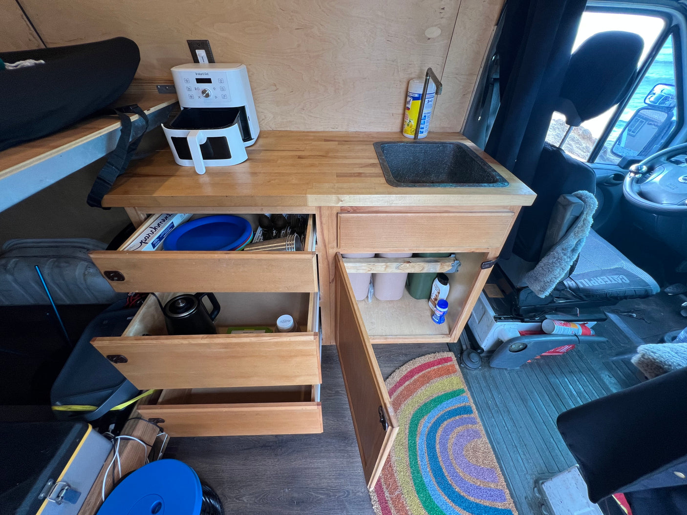 Inside an RV rental: a compact camper van kitchen with a sink, air fryer, and open drawers, ready for cooking on the road.