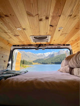 Serene RV rental interior looking out to a vast lake, green forests, & snow-capped mountains.