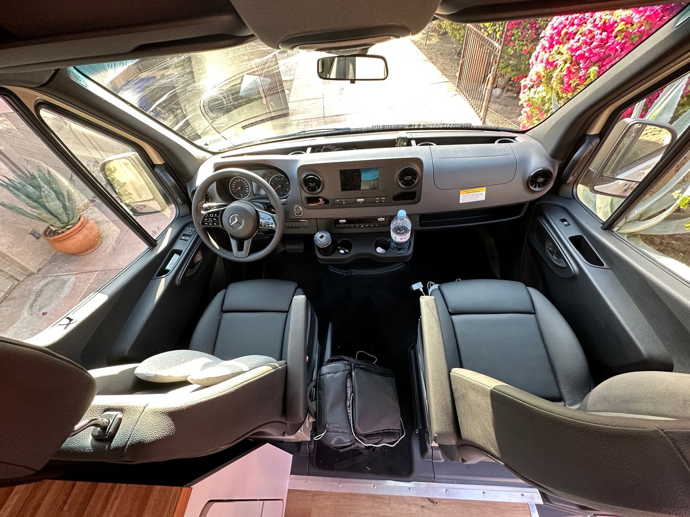 RV rental Mercedes Sprinter interior: forward view from back showing driver's cockpit, front seats, & exterior path with flowers. — photo 7