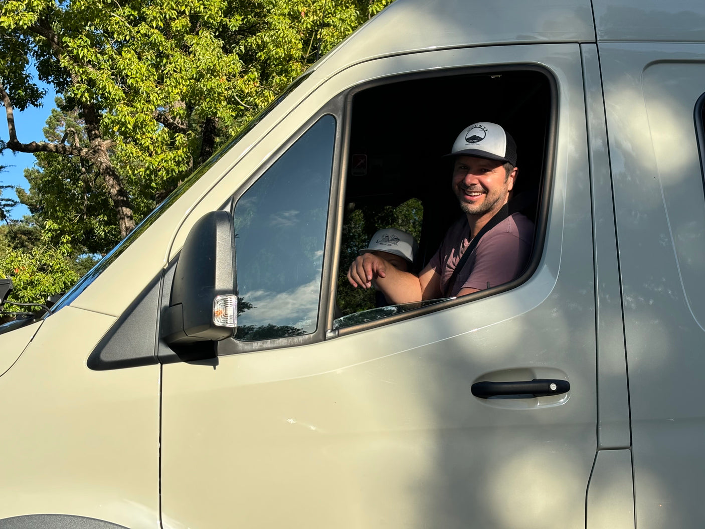 Smiling man and child in a light-colored camper van, perfect for an RV rental family trip.