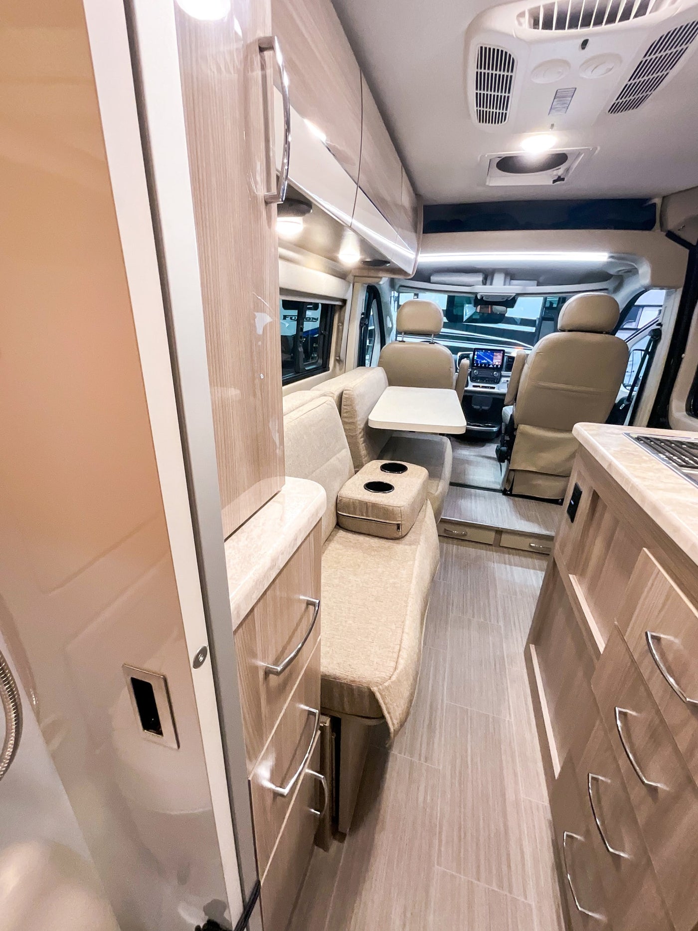 Inside a modern **rv rental**: light-toned interior with a cozy living area, dining table, kitchen counter, and front cab. — photo 7