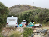 Vintage travel trailer (RV rental) and tent set up at a rustic campsite, complete with a picnic area and SUV. Ideal for nature escapes.