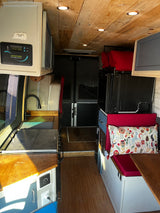 Step into this rv rental's interior: wooden ceiling, solar charge controller, compact kitchen, & cozy seating with a patterned pillow.