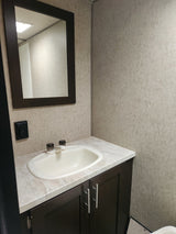 RV rental bathroom vanity with white sink, dark cabinets, modern mirror, and light textured walls.