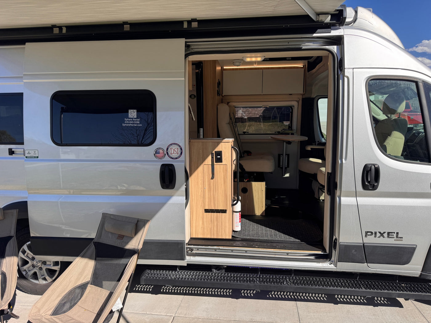 Explore this silver camper van rv rental! Side door open, showcasing a modern interior, extended awning, and outdoor chairs. — photo 6