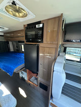 Spacious RV rental interior: bed, kitchenette with microwave & fridge, storage, and seating area. Ready for adventure!
