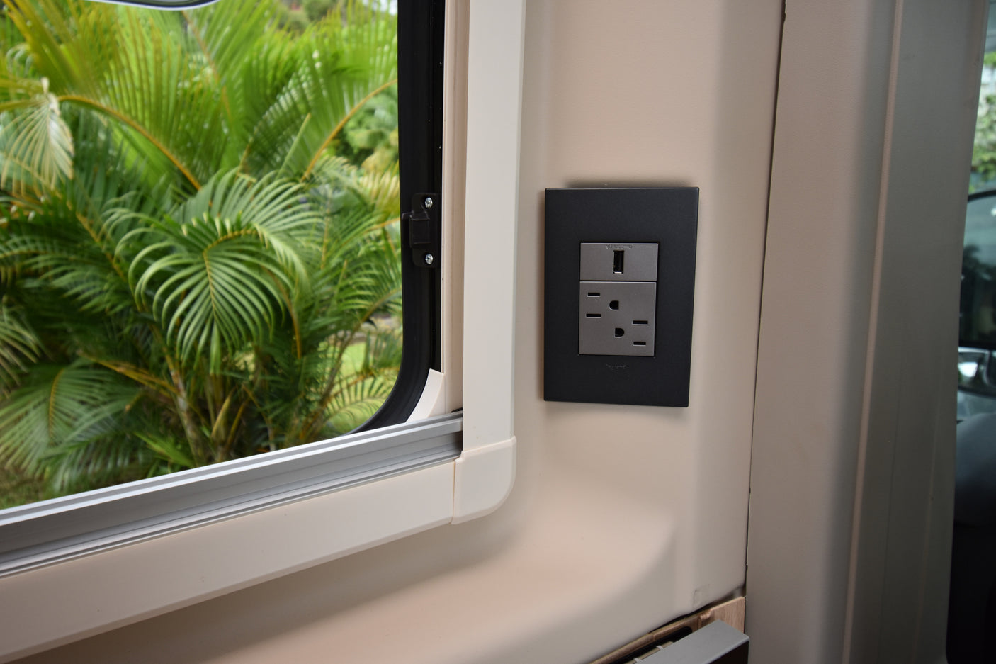Modern RV rental interior featuring a window with a lush green view and a convenient USB and AC power outlet.