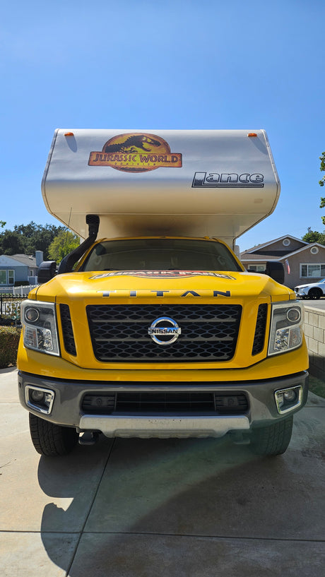 Front view of a vibrant yellow Nissan Titan truck with a Jurassic World-themed Lance truck camper, ideal for RV rental.
