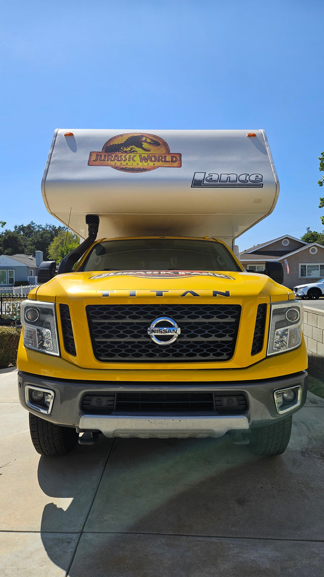 Front view of a vibrant yellow Nissan Titan truck with a Jurassic World-themed Lance truck camper, ideal for RV rental.