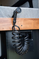 Black multi-setting spray nozzle on a coiled hose, part of an RV rental water system for convenient outdoor use.
