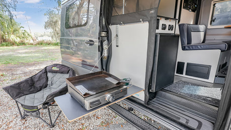 RV rental: Camper van featuring an outdoor griddle on a pull-out table, and a comfy camp chair for outdoor cooking.