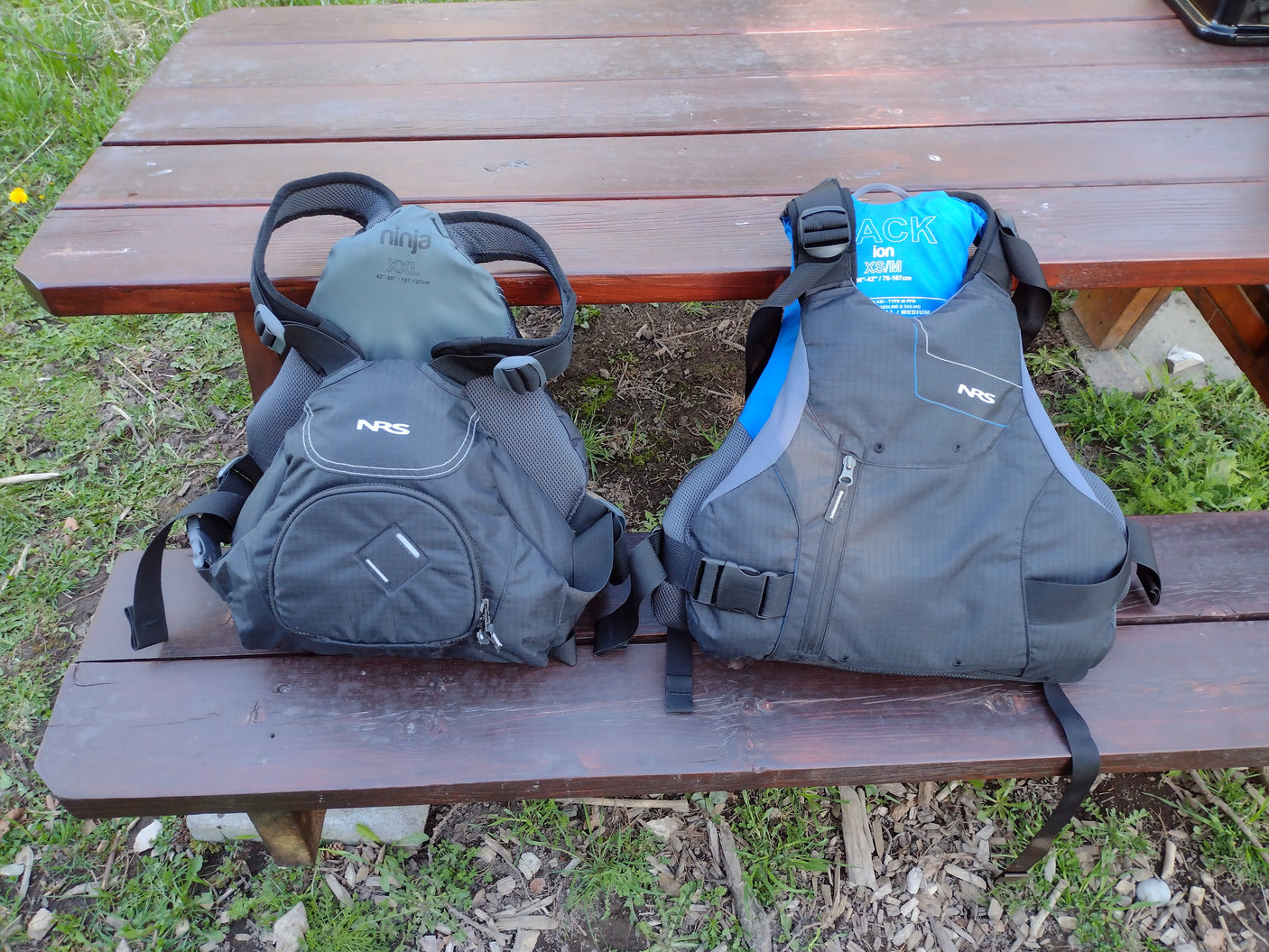 Two NRS PFDs (Ninja XXL, Ion XS/M) on a picnic table, essential water safety gear for your next rv rental trip.