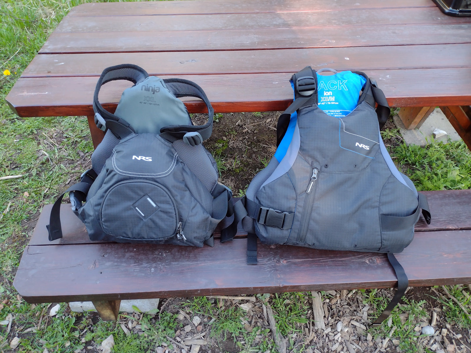 Two NRS PFDs (Ninja XXL, Ion XS/M) on a picnic table, essential water safety gear for your next rv rental trip.