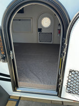 Inside a compact RV rental featuring an arched door, window blinds, fire extinguisher, and mesh storage net for travel.