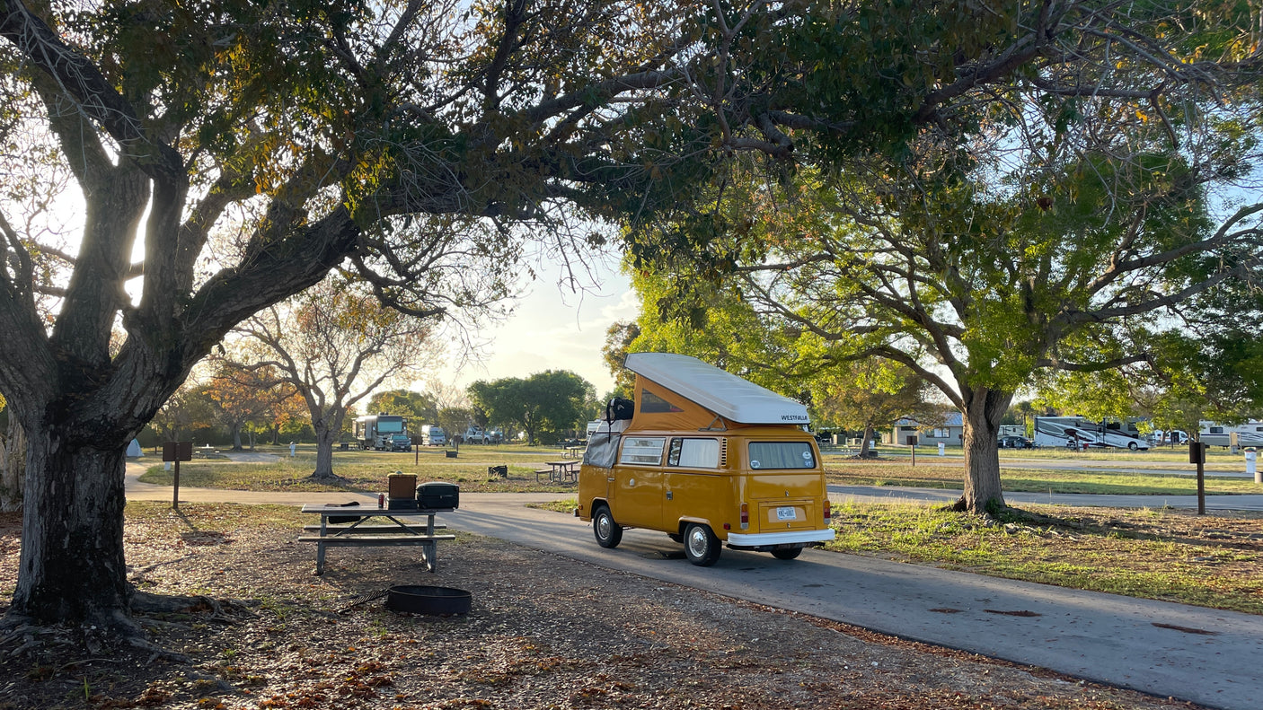 A classic yellow VW Westfalia camper van, perfect for an RV rental adventure, parked in a sunny campground.