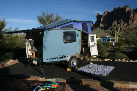 Enjoy desert adventures! This compact teardrop RV rental, with its pop-top tent, offers cozy camping amidst mountains & cacti.