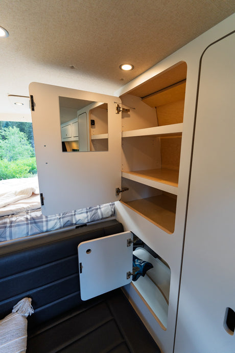 RV rental interior features a tall cabinet with shelves, a mirror on a door, and lower storage by the bed.