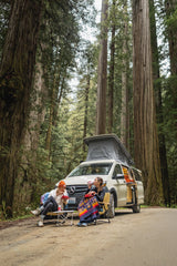 Enjoying an outdoor meal in front of an RV rental camper van, surrounded by giant redwood trees.