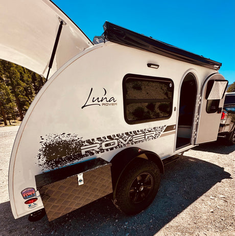 This off-road Luna Rover teardrop RV rental, with open hatches, is parked outdoors. Ready for your next adventure!