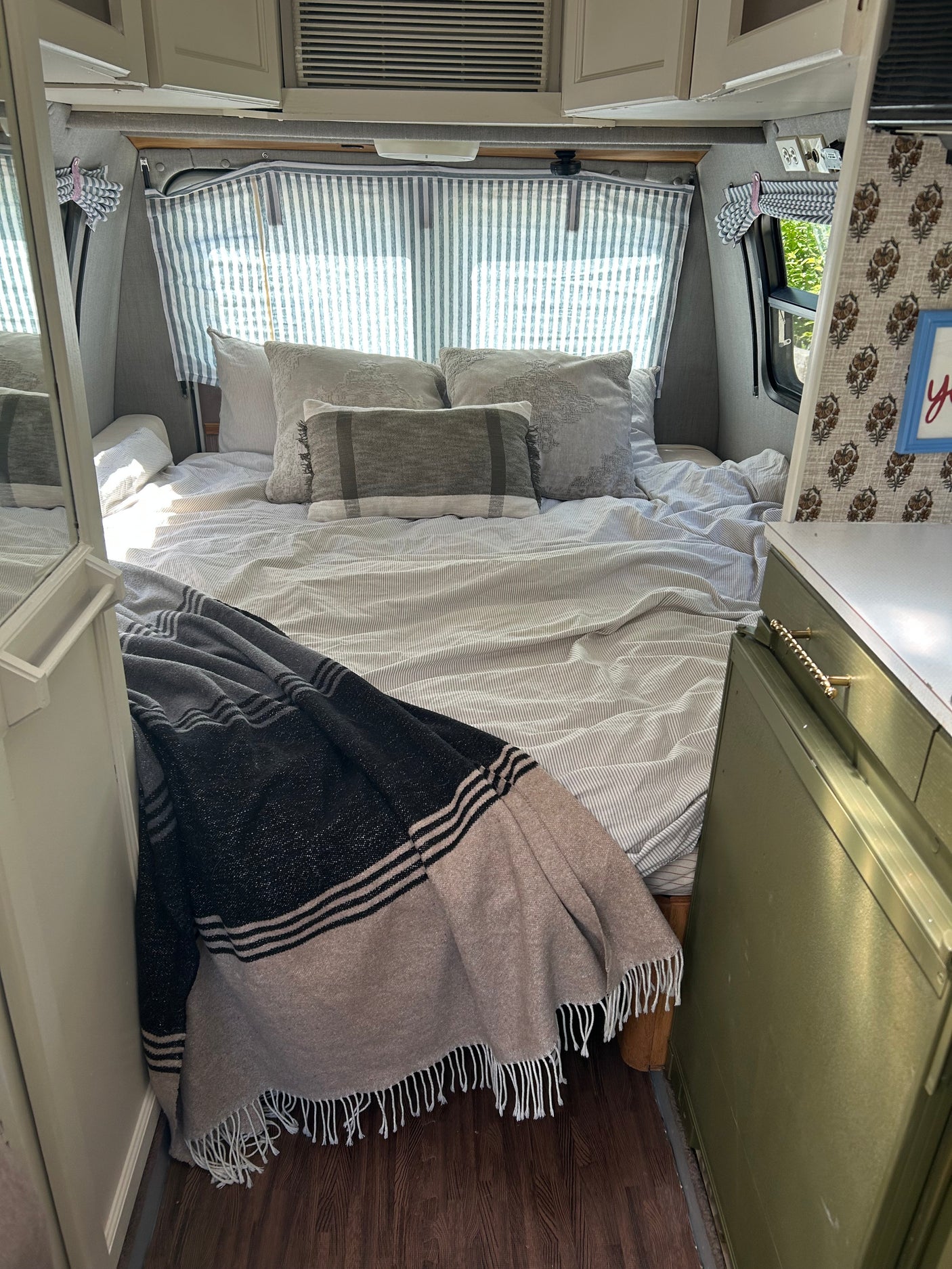 Cozy RV rental bedroom with striped bedding, fluffy pillows, and a comfy throw blanket, ideal for a relaxing getaway.
