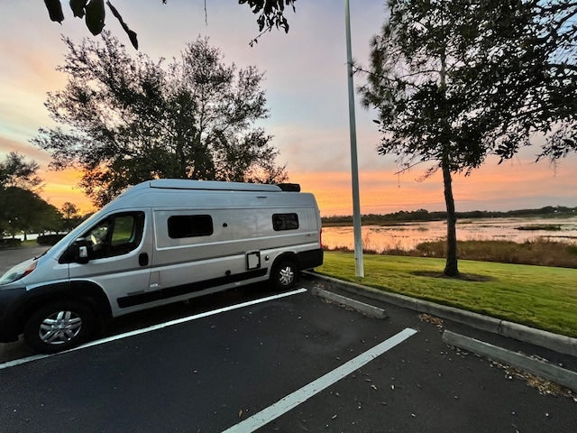 Scenic RV rental camper van parked by a tranquil lake, bathed in vibrant sunset colors. A perfect travel escape.