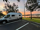 Scenic RV rental camper van parked by a tranquil lake, bathed in vibrant sunset colors. A perfect travel escape.