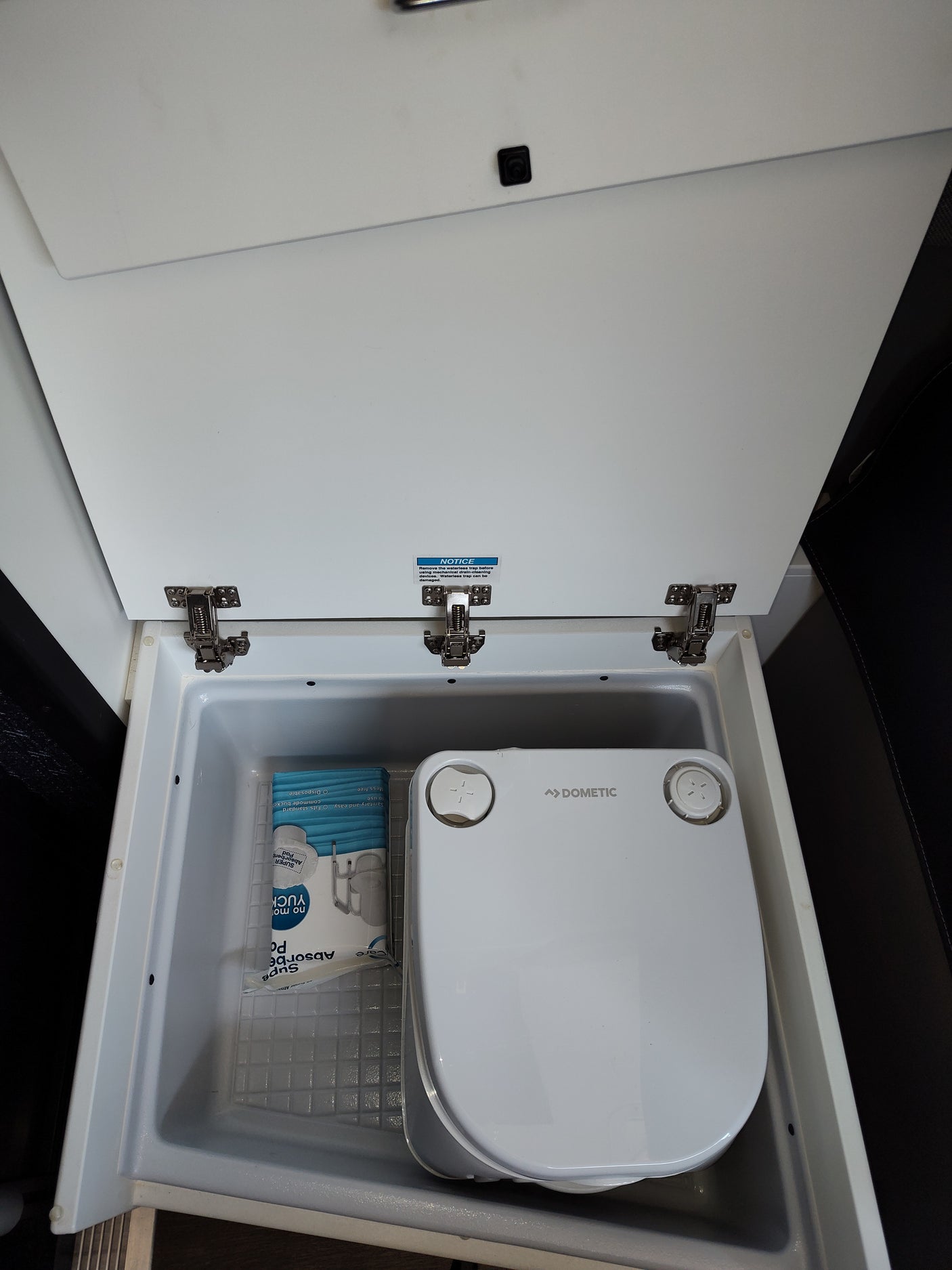 Inside an rv rental, a Dometic portable commode and absorbent pads are neatly stored, ready for use on the road.