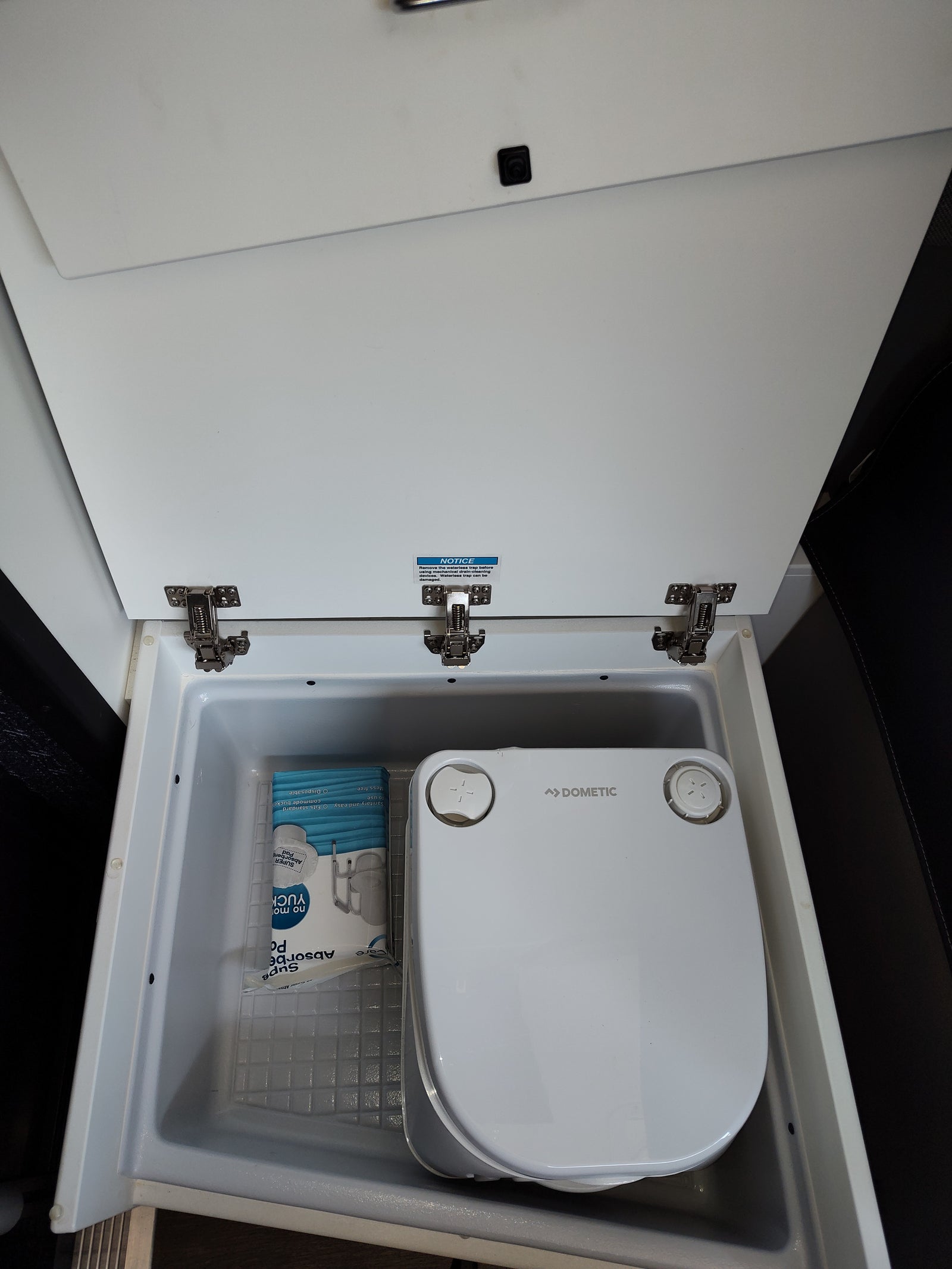 Inside an rv rental, a Dometic portable commode and absorbent pads are neatly stored, ready for use on the road.