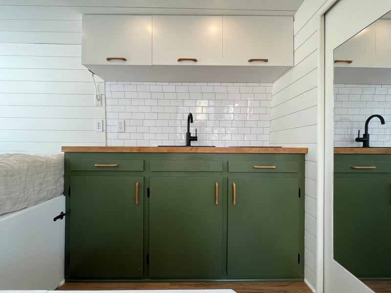Modern RV rental interior: green kitchen cabinets, white subway tile, wood counters/handles, shiplap walls, and compact bed. — photo 9