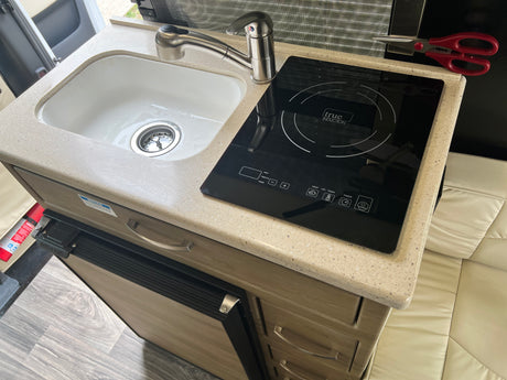RV rental kitchenette with sink, True Induction cooktop, and Nova Kool fridge. Ready for cooking on the go.