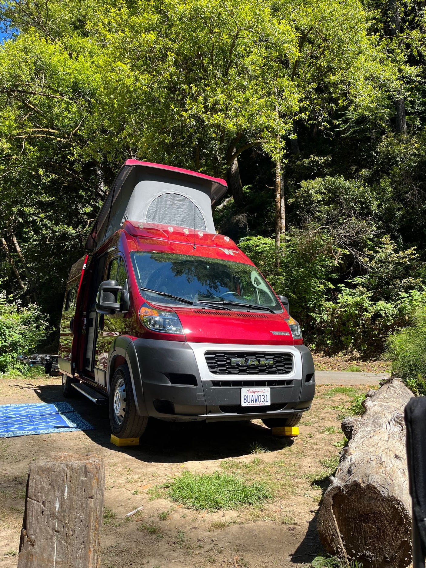 This red pop-top RV rental is perfectly leveled at a sunny campsite, ready for your outdoor adventure.