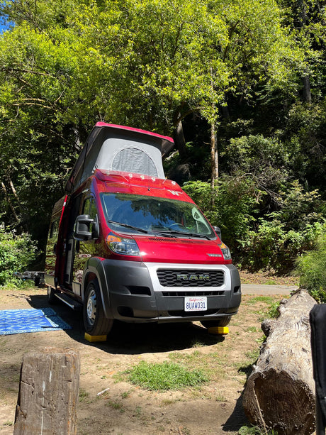 This red pop-top RV rental is perfectly leveled at a sunny campsite, ready for your outdoor adventure.