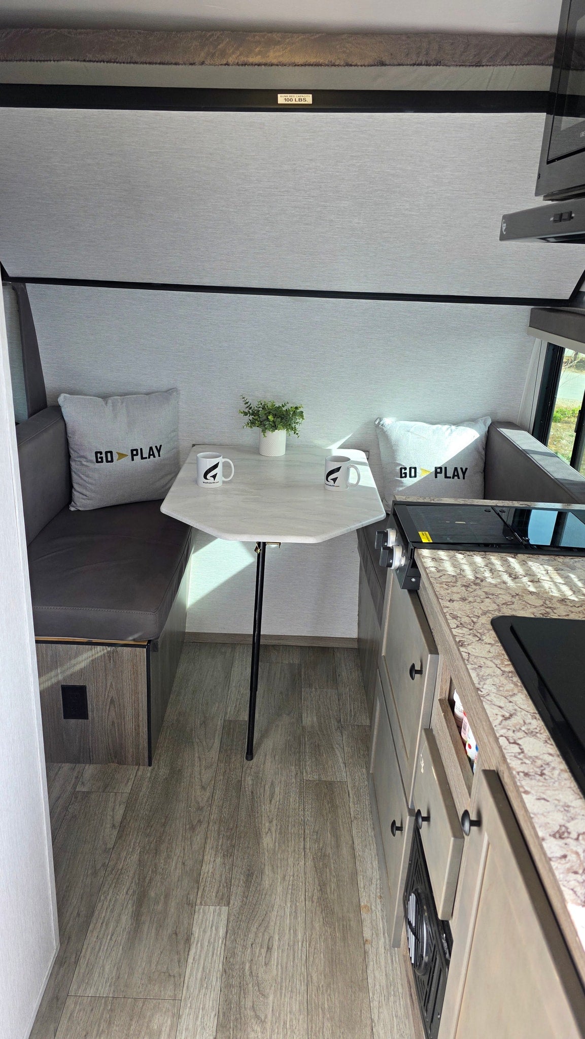 RV rental interior: dinette with 'GO PLAY' pillows, compact kitchen, and overhead bunk bed, ready for adventure. — photo 5