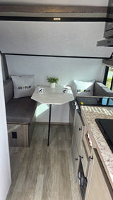 RV rental interior: dinette with 'GO PLAY' pillows, compact kitchen, and overhead bunk bed, ready for adventure.