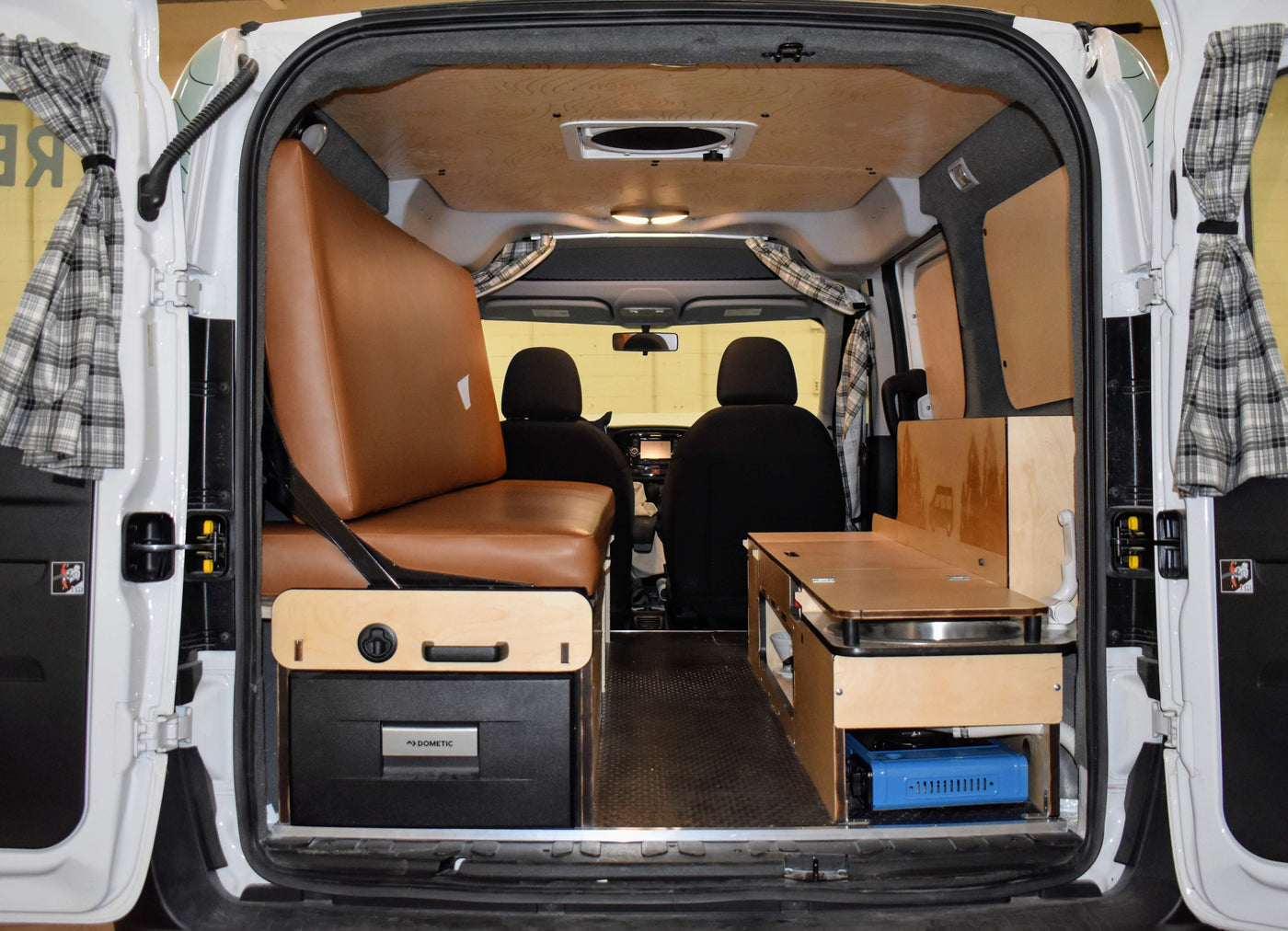 Inside an RV rental: Compact campervan conversion showing a brown bench-bed, Dometic fridge, and a functional kitchen. — photo 6