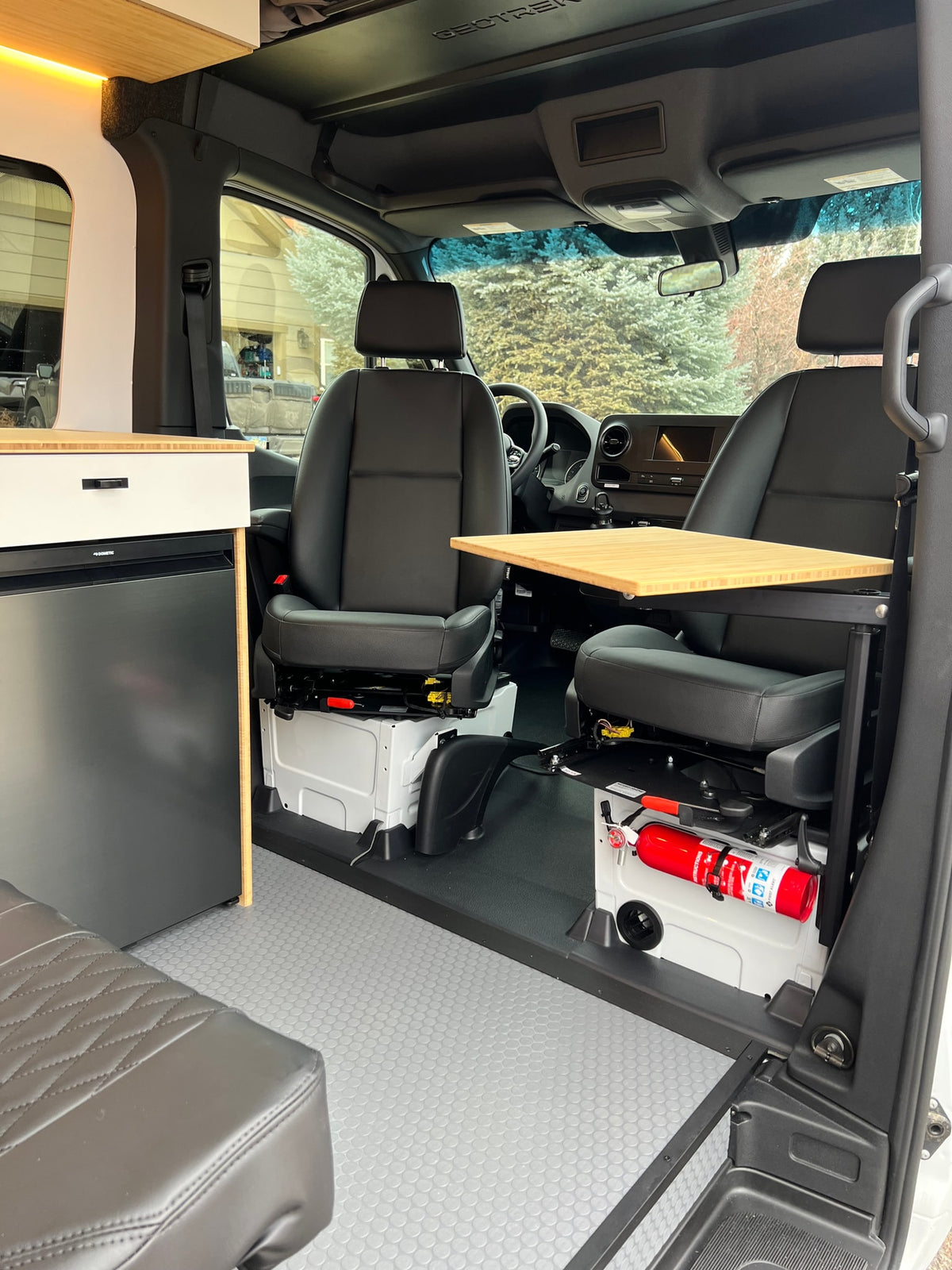 Inside an rv rental: swivel front seats, a versatile bamboo table, Dometic fridge, and safety gear. Perfect for road trips! — photo 12