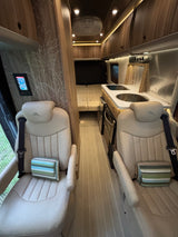 Step into this modern RV rental interior, featuring comfortable captain's chairs, a well-equipped kitchen, and cozy sleeping area.